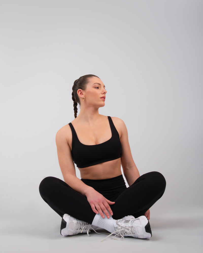 Femme en brassière de sport noire, assise au sol en position de repos après l'exercice.