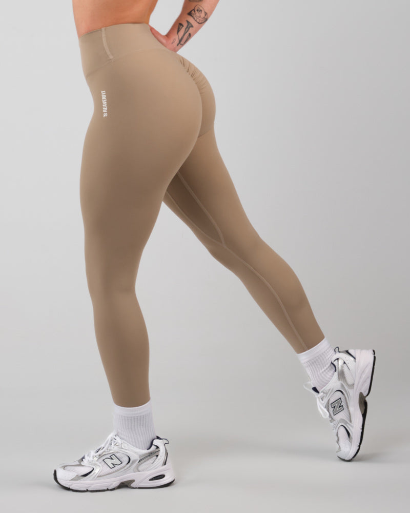 Vue de côté en action d'une femme portant des leggings de sport camel, mettant en avant la flexibilité et le soutien du tissu