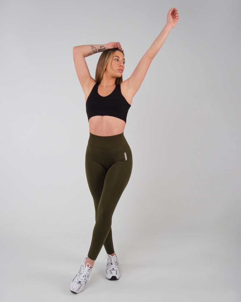 Vue latérale d'une femme portant le legging AMBER kaki, bras levés en étirement, soulignant la flexibilité et le confort du tissu.