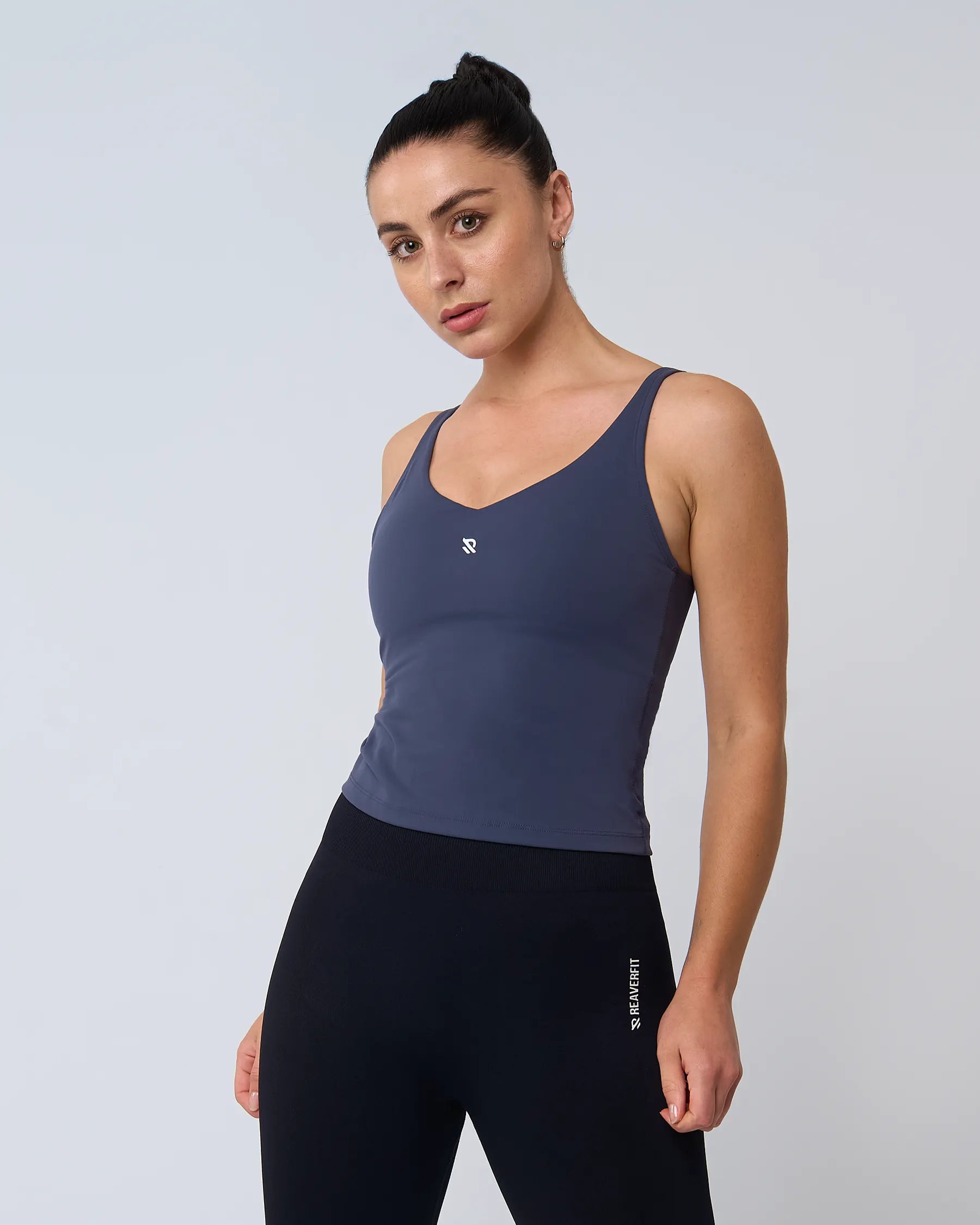 Femme en débardeur AURA bleu de Reaverfit, de côté, montrant la flexibilité du tissu, idéal pour le sport et les activités physiques.
