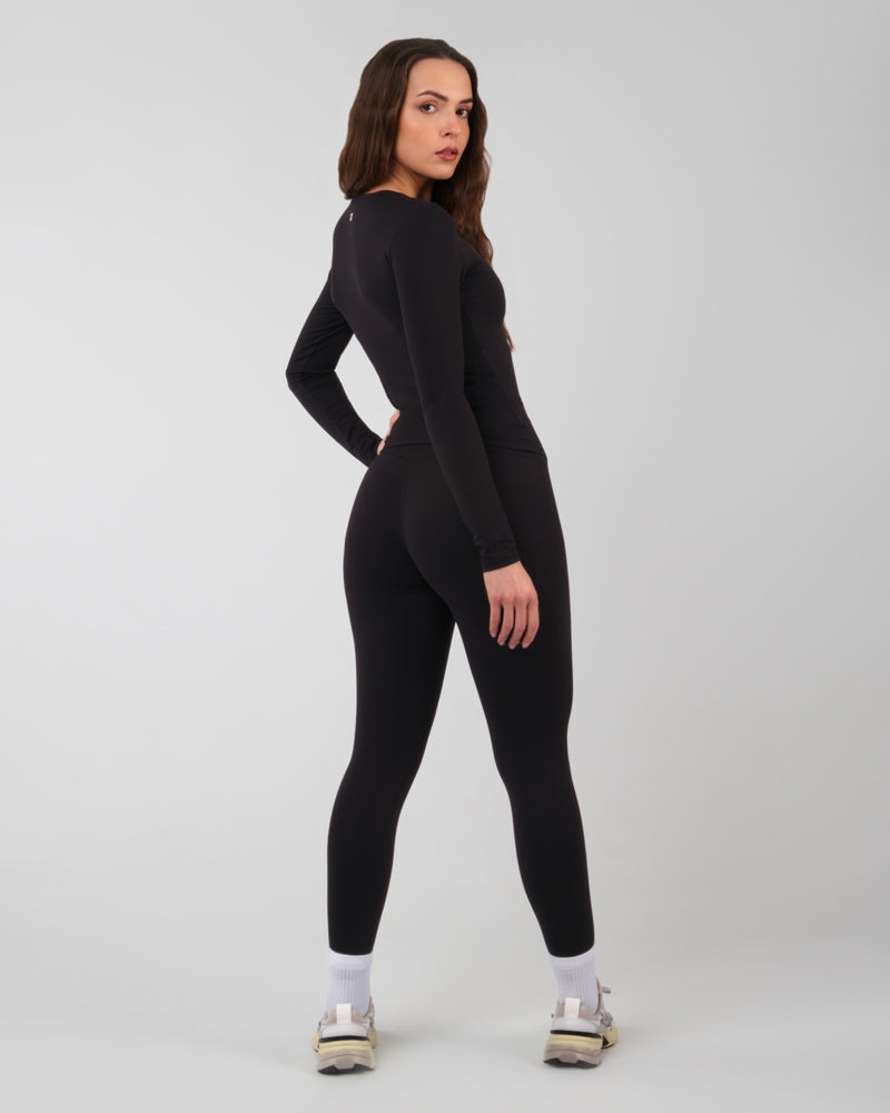 Arrière d'un haut à manches longues ALMA noir innovant et confortable sur une femme en salle de gym.