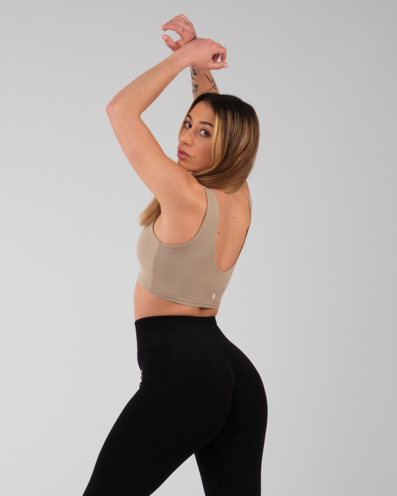 Brassiere sport Jane camel avec femme faisant un etirement des bras, mettant en evidence le confort et la flexibilite du tissu.
