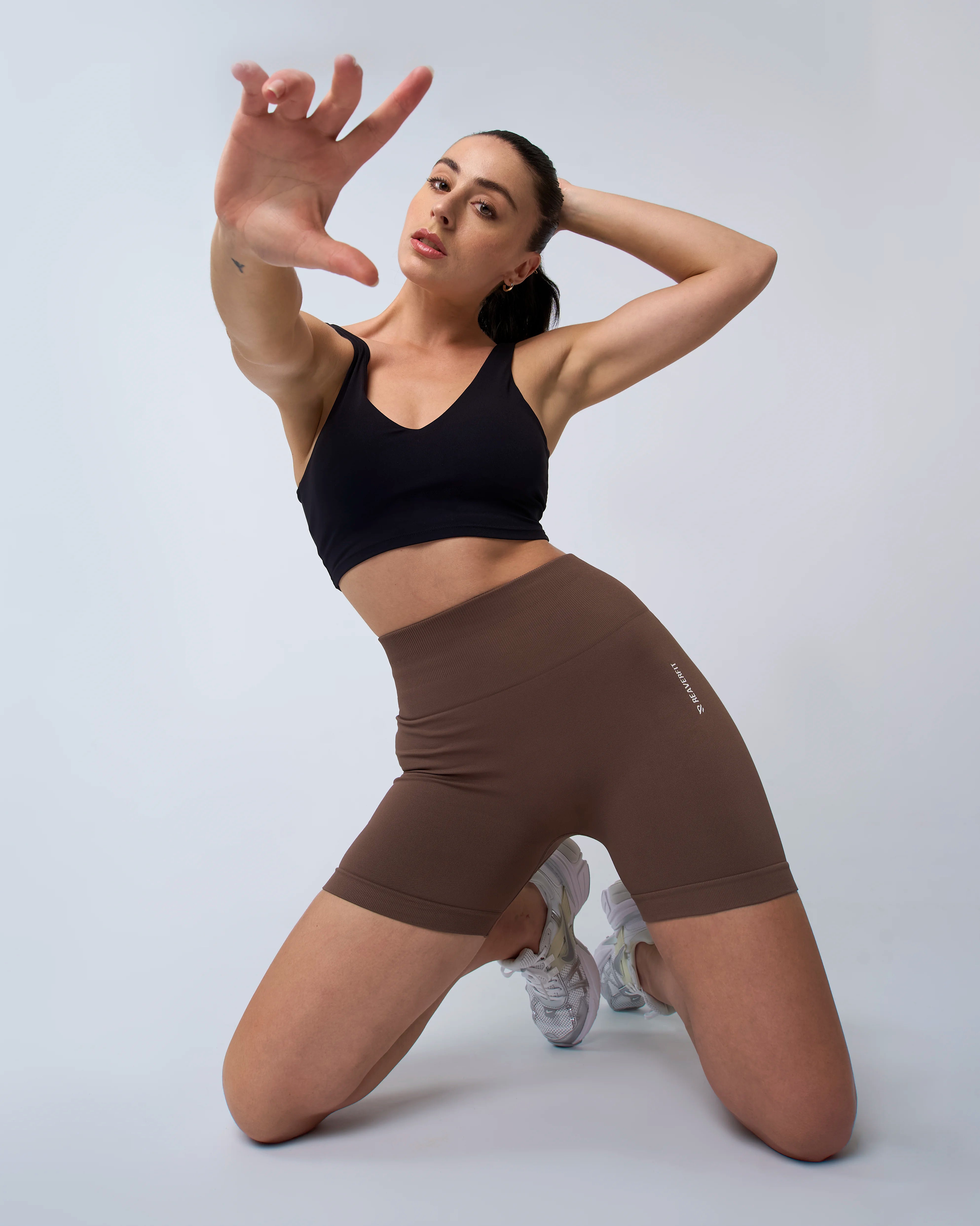 Femme accroupie en short sculpt mocha, taille haute, effet push-up.