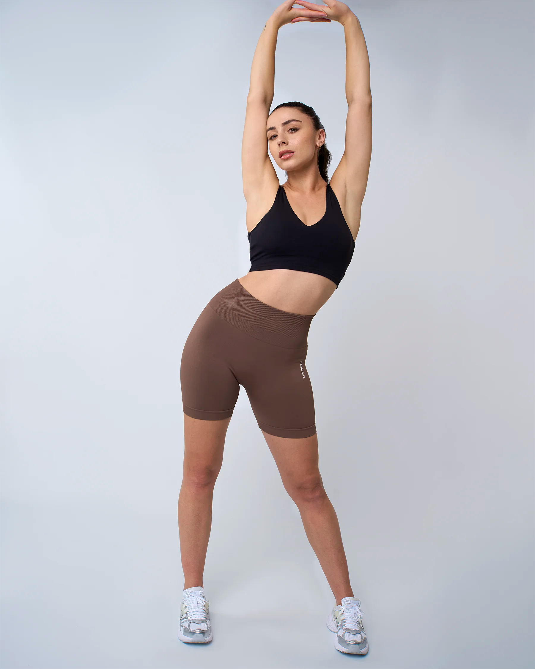 Femme debout bras levés en short sculpt mocha, coupe ajustée et extensible.