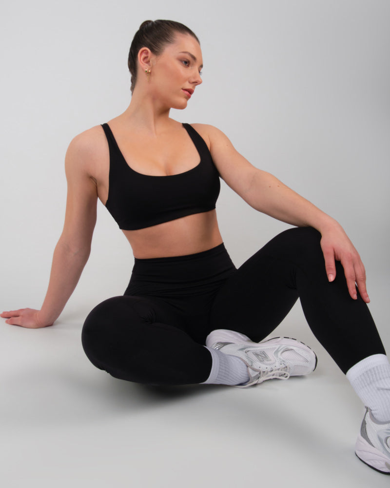 "Vue de trois-quarts d'une femme debout en brassière de sport noire et leggings, mains sur les hanches, prête à s'entraîner.