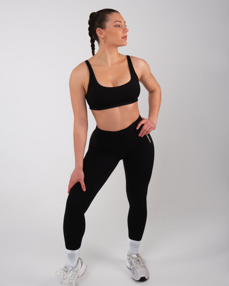 Femme en brassière de sport noire et leggings assortis, adoptant une pose sportive, prête pour l'entraînement