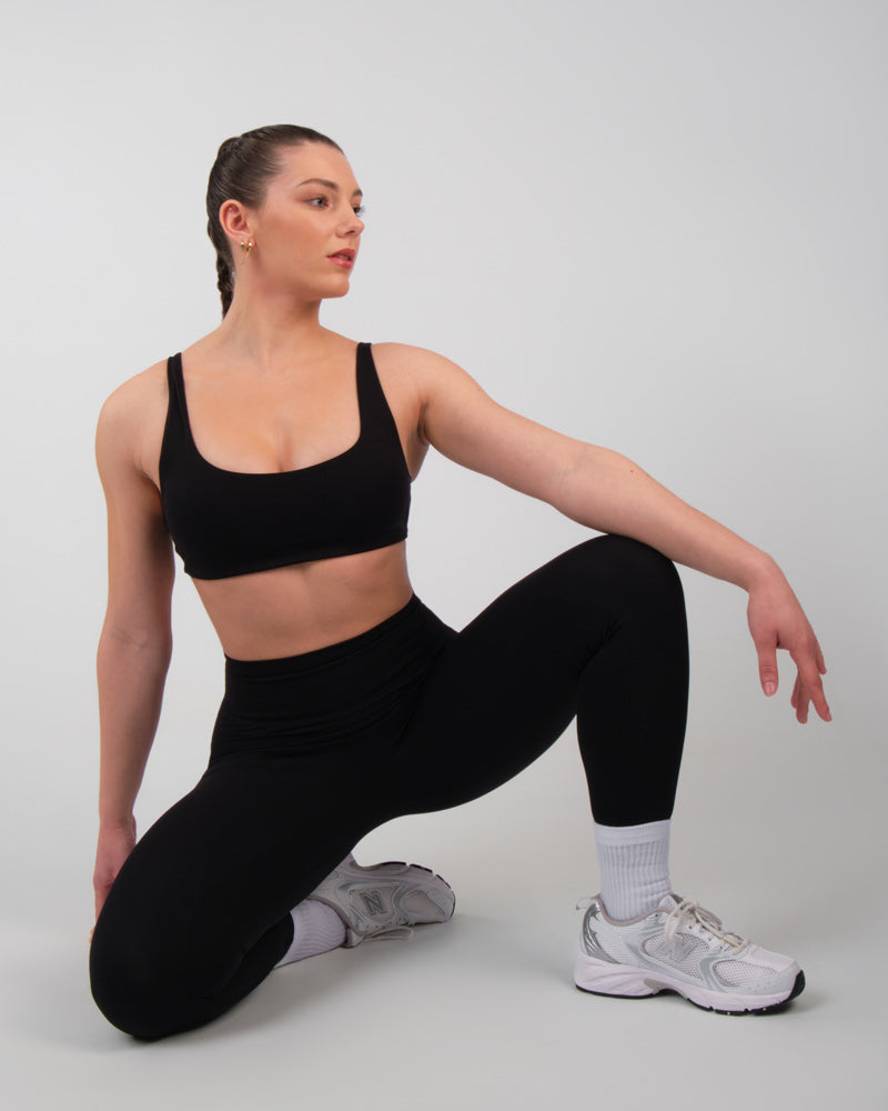 Femme en brassière de sport noire et leggings, accroupie dans une pose dynamique de préparation à l'exercice