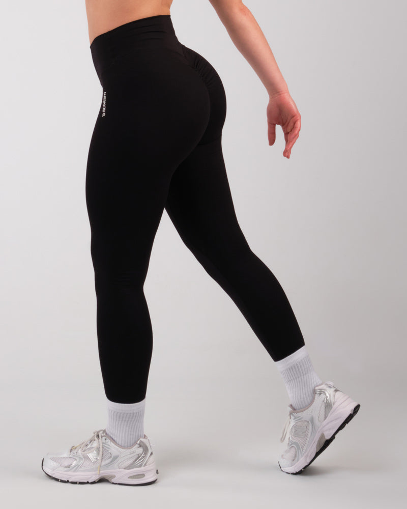 Vue de profil gauche d'une femme en leggings noirs sportifs, en marche, accentuant la silhouette athlétique.
