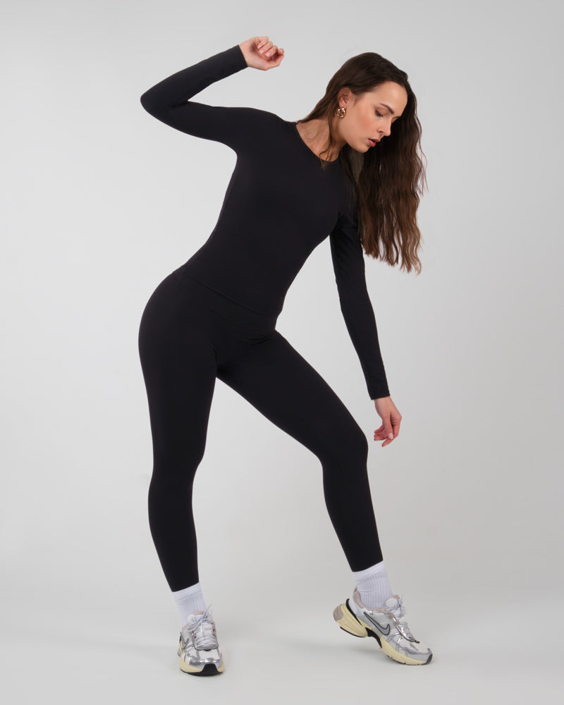 Profil d'une femme portant le haut à manches longues ALMA noir, flexible pour l'entraînement et la musculation.
