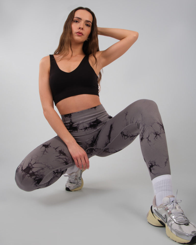 Femme en position accroupie de côté, portant un legging de sport gris push-up, démontrant la résistance et le confort du legging en position basse.
