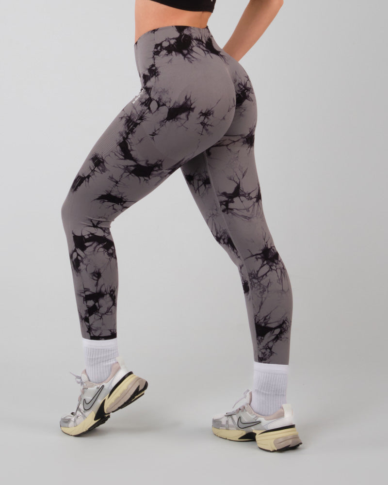 Vue de trois quarts arrière d'une femme en mouvement, portant un legging de sport gris push-up, illustrant la flexibilité et la fonctionnalité du legging lors de mouvements actifs.