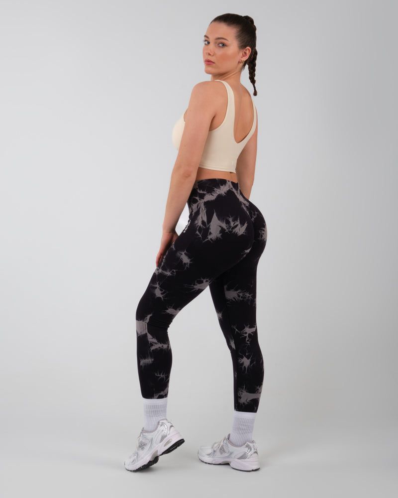 Femme de dos portant un legging de sport noir onyx push-up, en position de flexion du genou, accentuant la fonctionnalité et le soutien du legging.