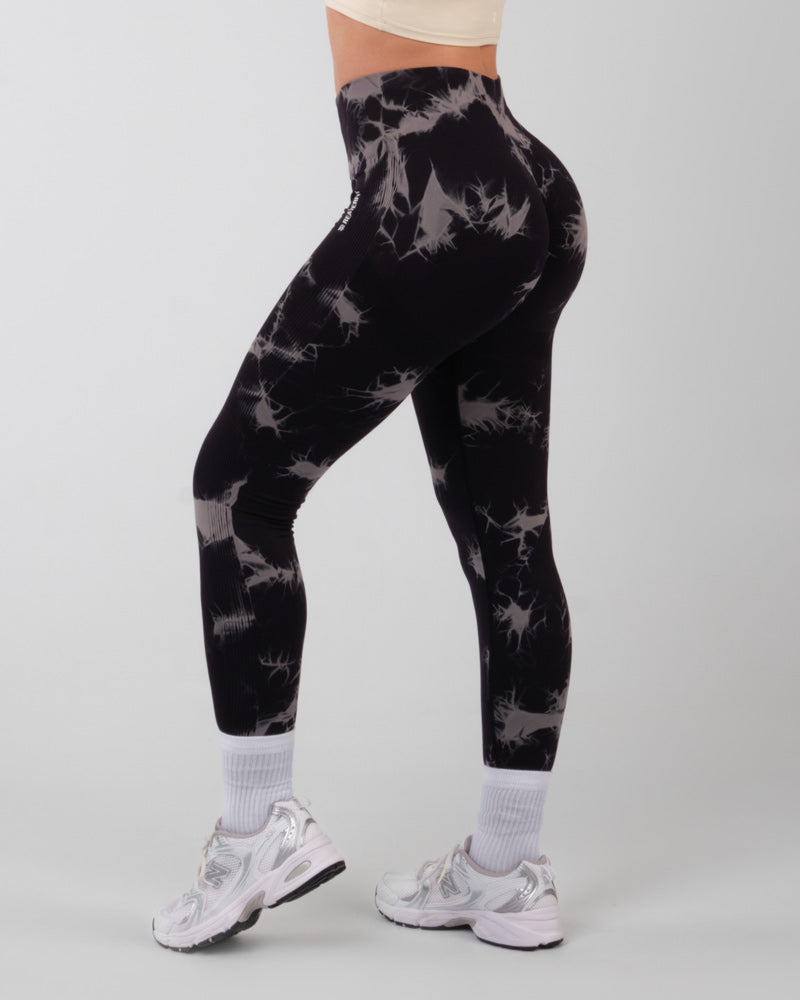 Femme de dos portant un legging de sport push-up noir onyx avec motif tye-die blanc, en position debout, montrant la coupe et le design du legging.