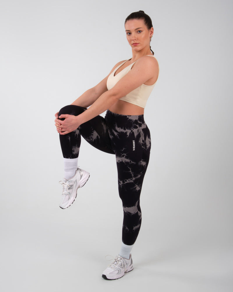 Vue de trois quarts arrière d'une femme portant un legging de sport push-up noir onyx avec des motifs tye-die blancs, démontrant la flexibilité et le style du vêtement.