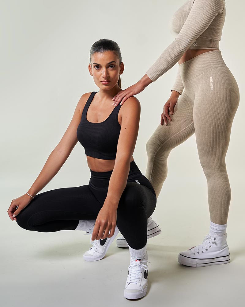 2 jeunes femmes portants de beaux ensembles de sport noir et beige sportswear Brassière de sport confortable et réglable, conçue pour un soutien optimal pendant l'entraînement